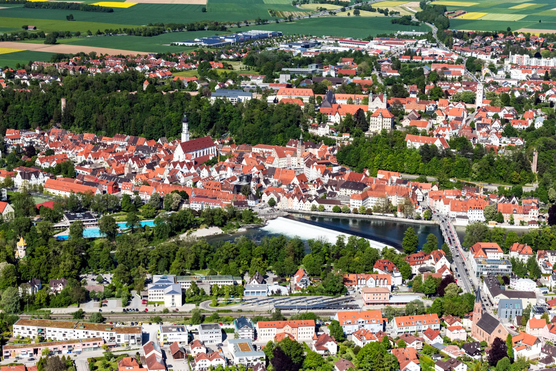 Luftaufnahme von Landsberg am Lech mit Altstadt, Stadtpfarrkirche, Lechwehr und umliegender Landschaft bei klarem Wetter.