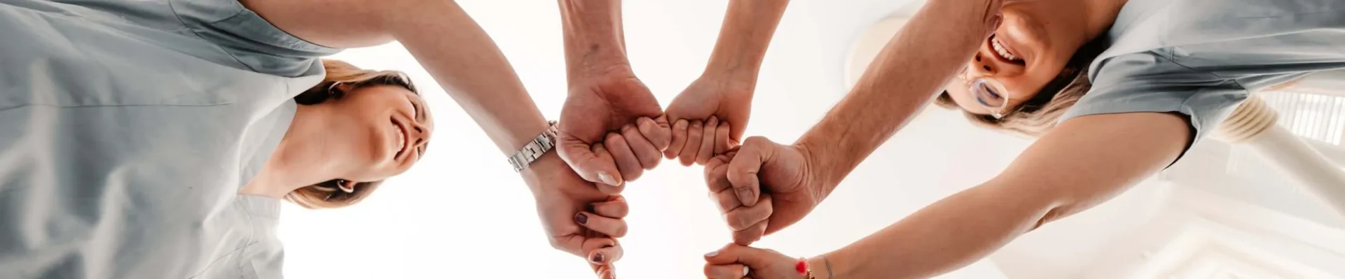 Das Team des hauseigenen Meisterlabors der Zahnarztpraxis zeigt Teamgeist mit geballten Fäusten im Kreis – Ansicht von unten.