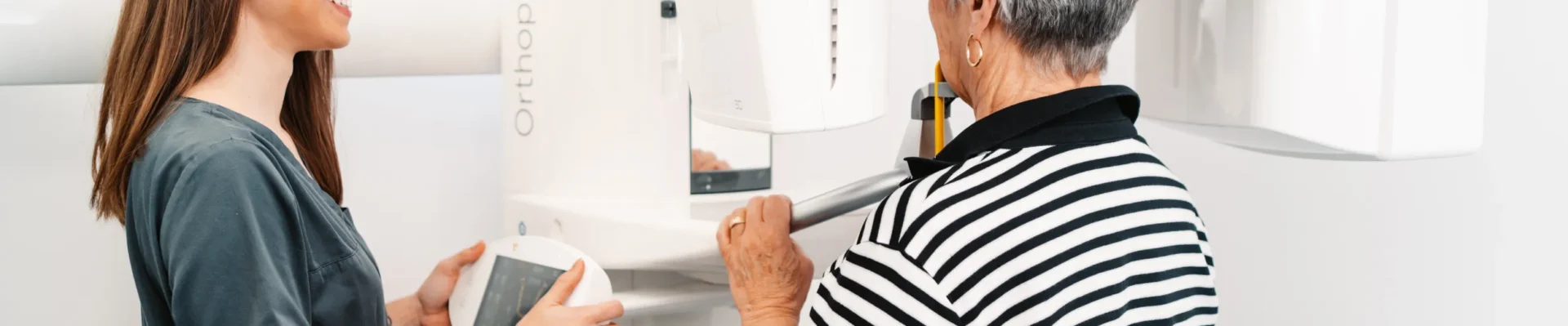 Zahnmedizinische Fachkraft weist eine Patientin in die richtige Positionierung am digitalen Röntgengerät Orthophos SL ein.