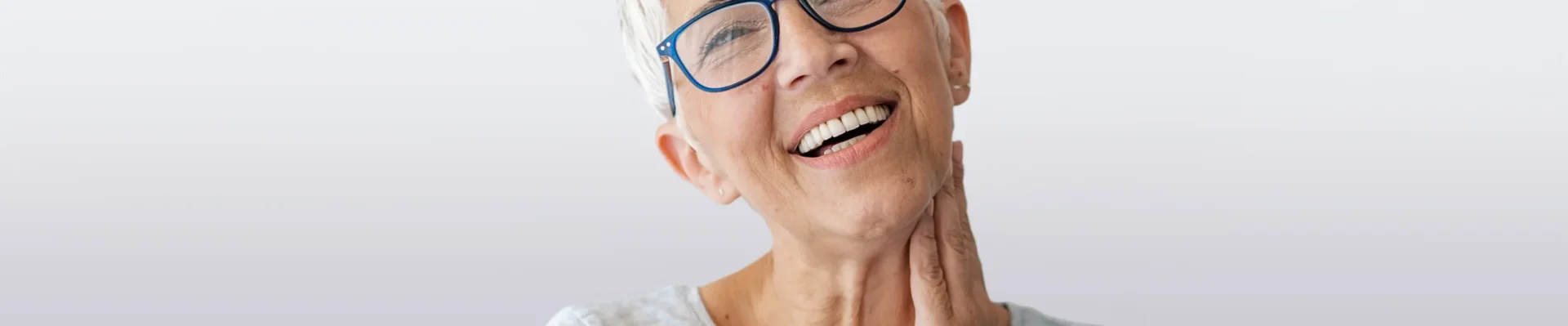 Nahaufnahme einer zufriedenen Patientin mit Brille lächelt und zeigt ihre Zähne.
