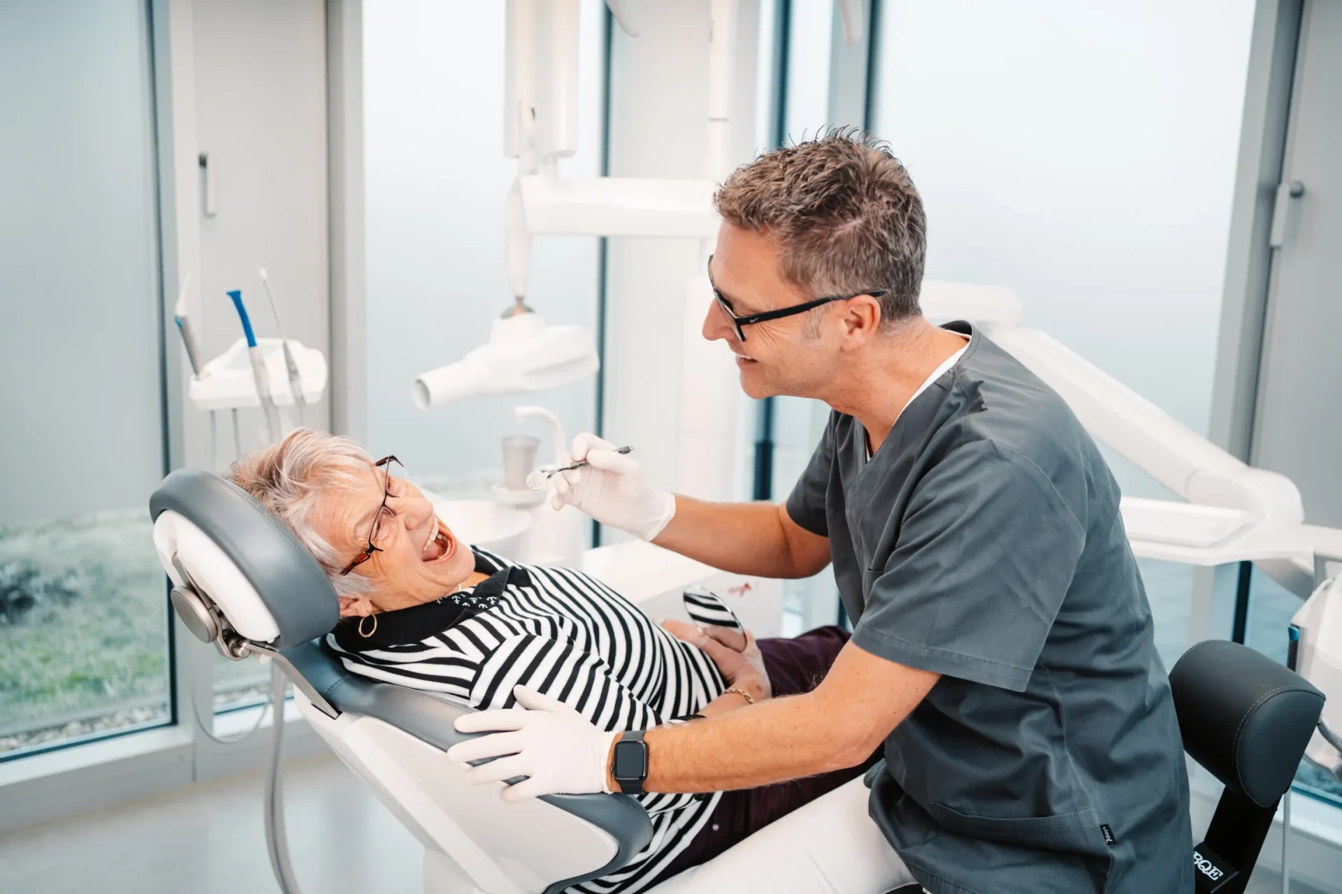 Zahnarzt untersucht einer älteren Patientin auf dem Behandlungsstuhl bei Dr. Bayer & Kollegen in Landsberg.