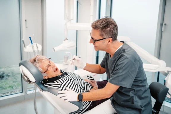 Zahnarzt untersucht einer älteren Patientin auf dem Behandlungsstuhl bei Dr. Bayer & Kollegen in Landsberg.