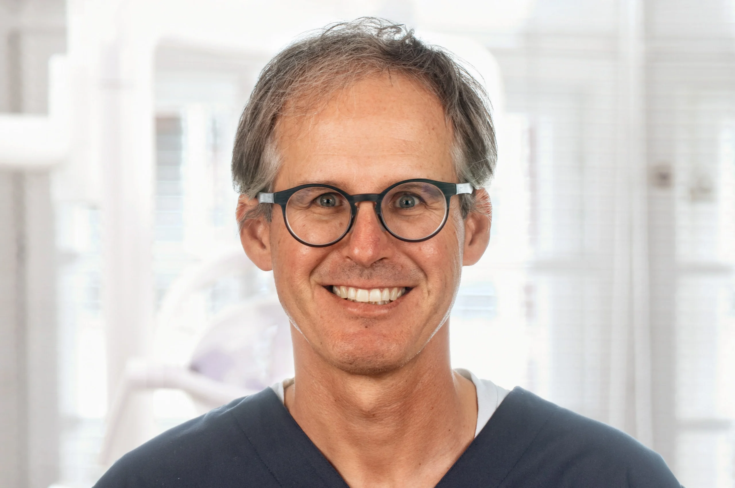 Porträt von Dr. Frank Kistler mit dunklem Kasack und freundlichem Lächeln – Zahnarzt bei Dr. Bayer & Kollegen in Landsberg, spezialisiert auf Oralchirurgie und Vollnarkose-Behandlungen.