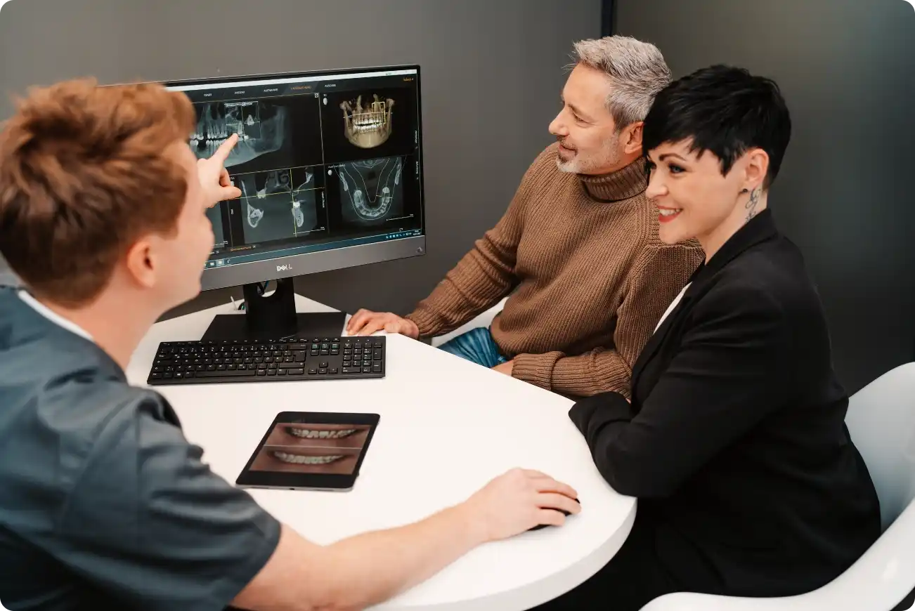 Zahnarzt zeigt einem Paar anhand eines digitalen Röntgenbilds die geplante Implantatversorgung – moderne Beratung in der Zahnarztpraxis Landsberg.