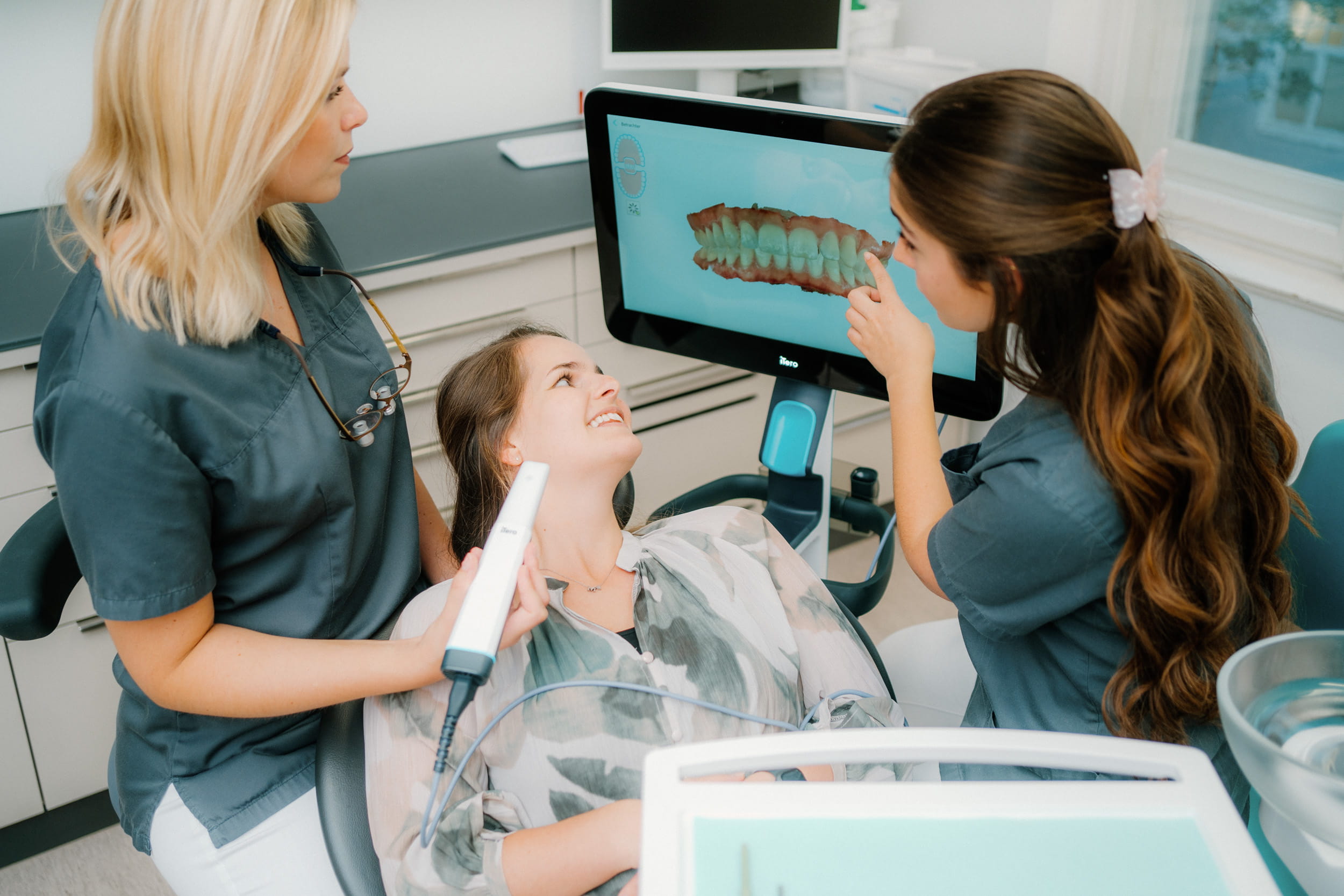 Zahnärztinnen nehmen mit einem Intraoralscanner einen digitalen Abdruck, das 3D-Modell der Zähne ist auf dem Bildschirm zu sehen.